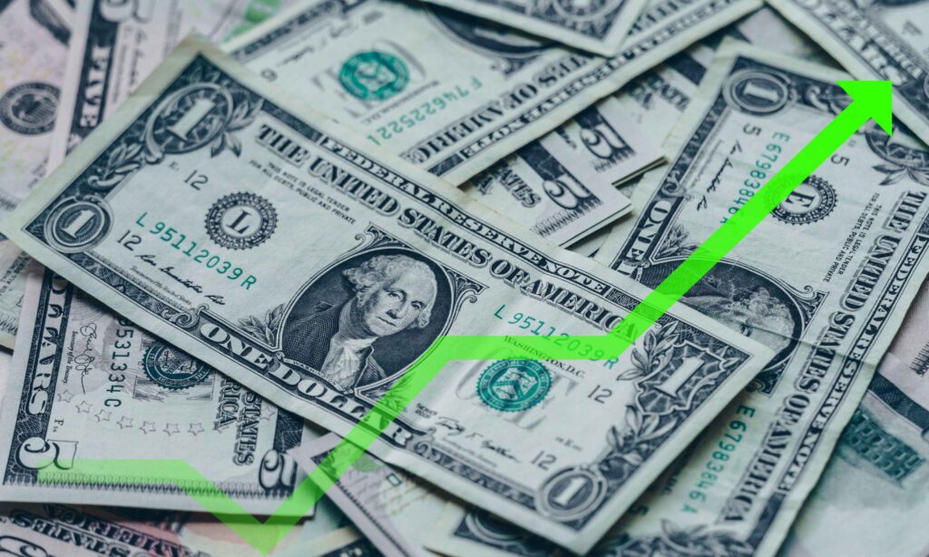 Notas de dólar americano com uma seta verde para cima, indicando crescimento financeiro. 1. Alta do dólar à vista, com investidores atentos a um possível acordo comercial.2. Dólar em alta, enquanto investidores monitoram negociações de um acordo comercial.3. Aumento do dólar, com foco dos investidores em um potencial acordo de comércio.4. Dólar se valoriza, à medida que investidores observam as tratativas de um acordo comercial.5. Valorização do dólar, com investidores de olho nas negociações de um acordo comercial.  Dólar fecha em alta de 0,53% a R$ 5,47 com cenário internacional e riscos fiscais