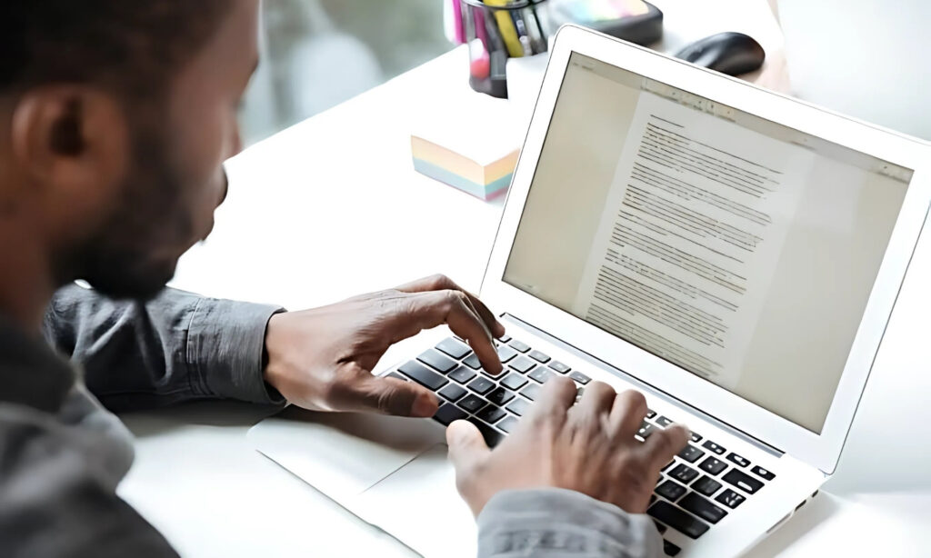 Pessoa digitando em um laptop com um documento na tela.  1. Homem digitando em um laptop, concentrado em seu trabalho como redator, com a tela iluminada à sua frente.  2. Um redator focado, digitando em seu laptop, cercado por anotações e ideias para seus textos.  3. Homem trabalhando em um laptop, escrevendo como redator, com expressão de concentração e criatividade.  12 Profissões com Flexibilidade no Trabalho para um Equilíbrio Ideal