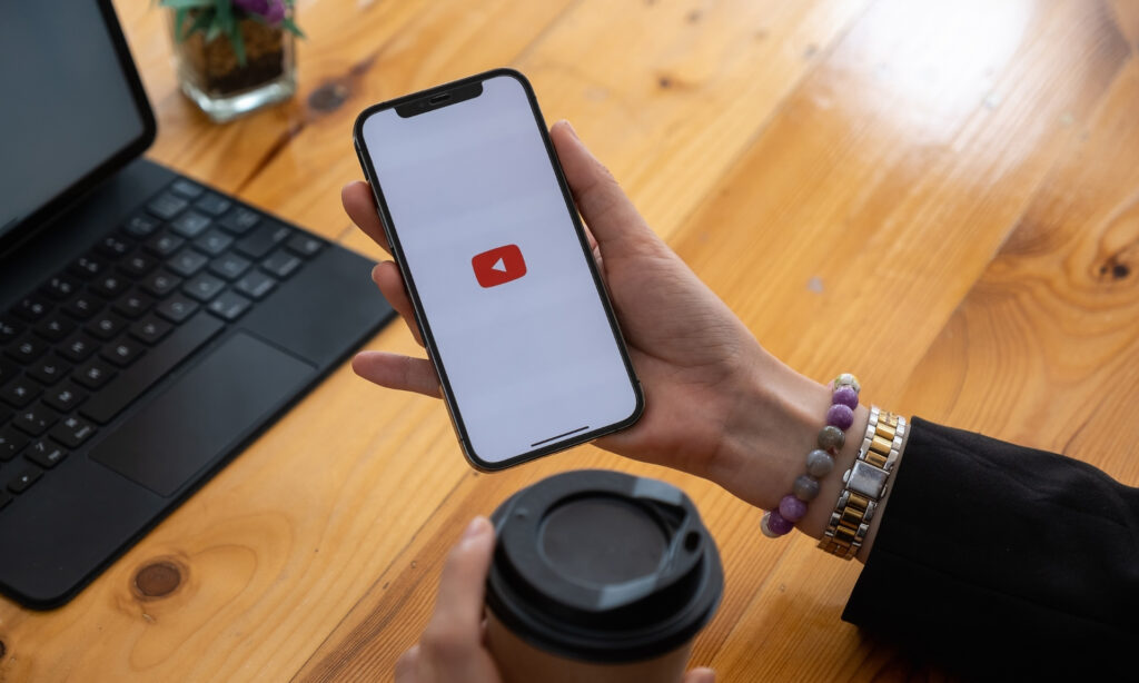 Como Ganhar Renda em Dólar e Proteger Seu Dinheiro da Alta da Moeda Imagem de uma mão segurando um celular com o logo do YouTube na tela, ideal para criar um canal no YouTube. Arte envolvente e tecnologia em foco. Como Ganhar Renda em Dólar e Proteger Seu Dinheiro da Alta da Moeda
